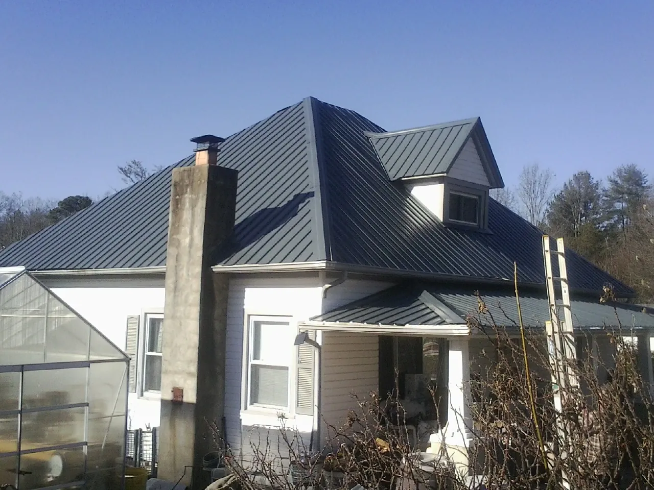 Dark blue standing seam metal roof on a white farmhouse with dormer — Slate & Tile Roof Repair by Roofing Brothers in Hunker