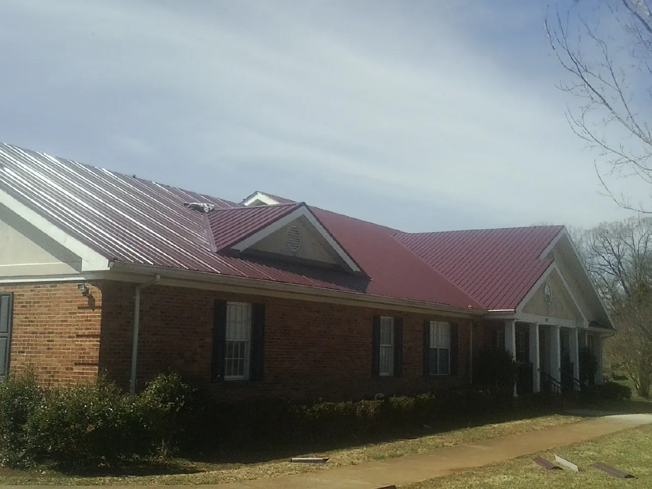 Red metal roof with gabled entries on a long brick building, from a Hail Damage Roof Repair job in Hunker