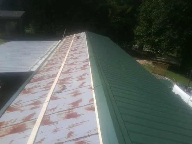 Old rusted panels beside newly installed green metal roofing — Wind Damage Roof Repair by Roofing Brothers in Hunker