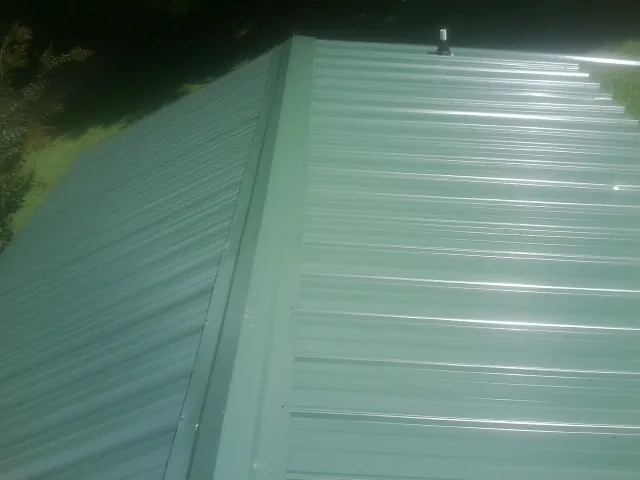 New green metal panels meeting at the ridge of a roof — Flat Roof Repair work by our crew in Hunker