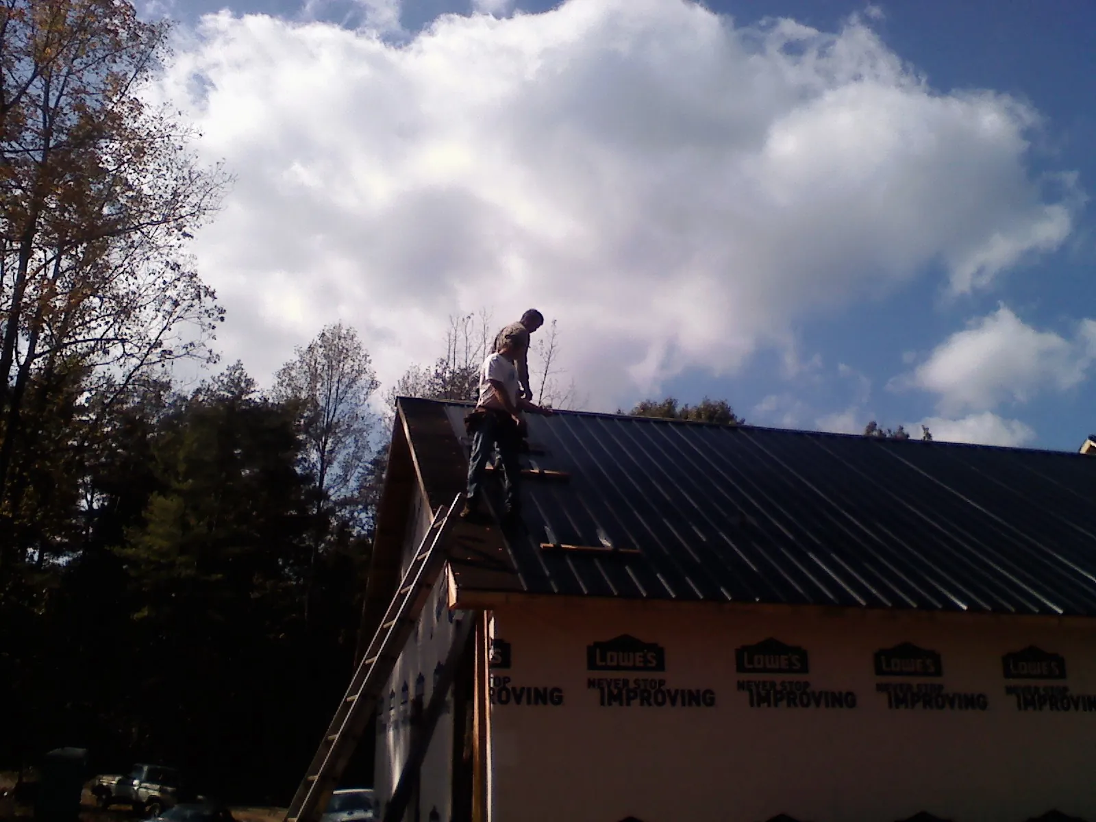 Roofer fastening dark metal panels high against a cloudy sky, from a Roof Inspection job in Hunker