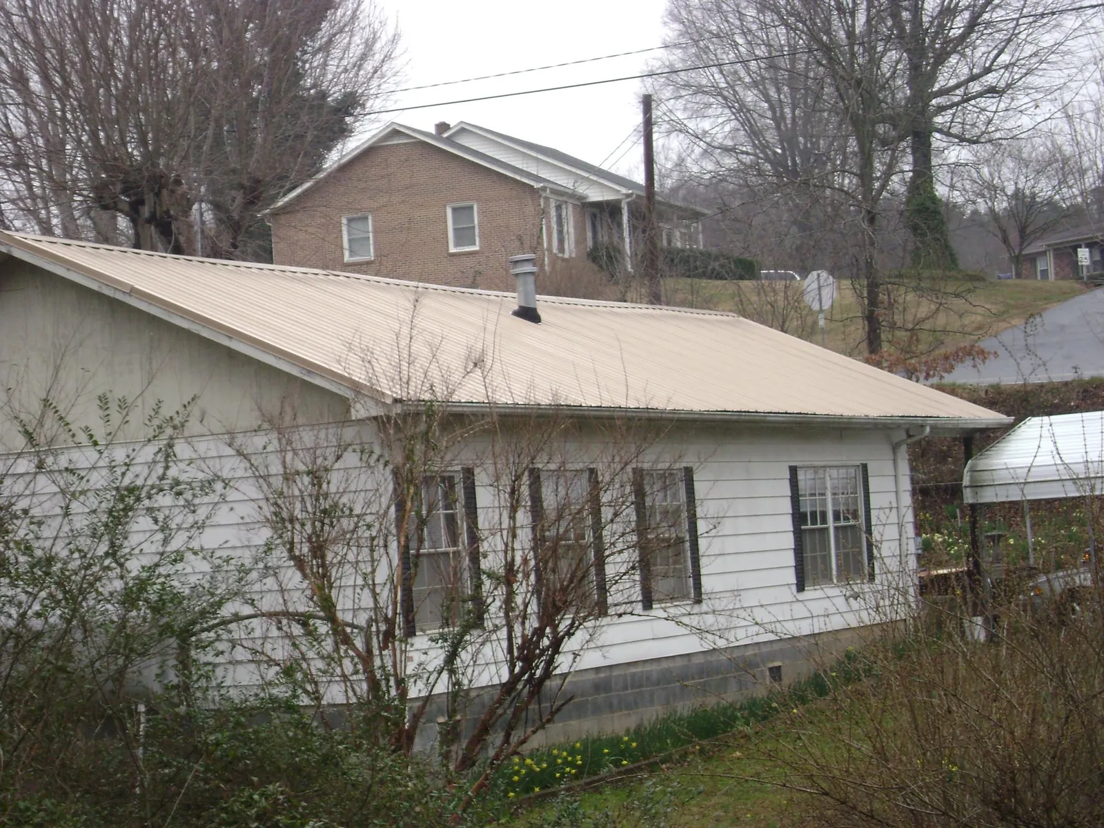 Tan metal roof on a white sided house set into a hillside — Commercial Roofing by Roofing Brothers in Hunker
